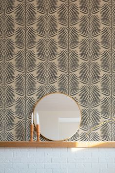 a mirror sitting on top of a wooden shelf next to a wallpaper covered in leaves