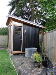 a small backyard shed with a tub in the yard next to it and some flowers