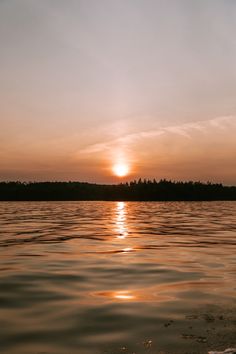 the sun is setting over water with trees in the background