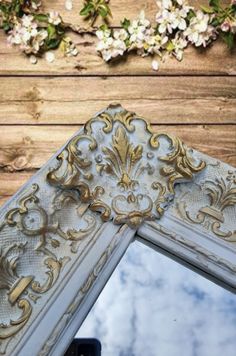 an ornate mirror is shown against a wooden wall with flowers growing on the side and behind it