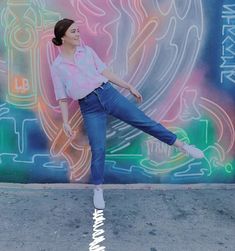 a woman standing on one leg in front of a colorful wall with writing and graffiti