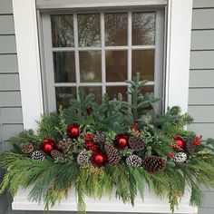 a window sill decorated with pine cones, evergreen and red ornaments in front of a house