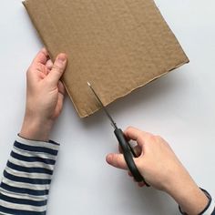 a person cutting out a piece of cardboard with a pair of scissors on top of it