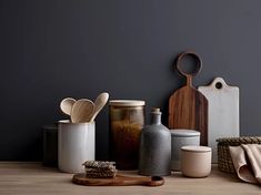 various kitchen utensils are arranged on a wooden table with a gray wall in the background