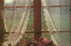 the window is covered with white lace and pink flowers in front of an open curtain