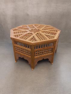 an octagonal wooden table with intricate carvings on the top and sides, sitting against a gray wall