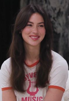 a woman with long hair sitting down and smiling