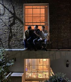 three people sitting on a window sill at night