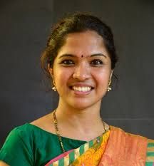 a woman in a green and orange sari smiles at the camera with her hand on her hip