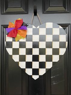 a heart shaped door hanger with a bow on it's side, in front of a black and white checkered door