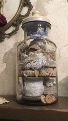 a glass jar filled with lots of different types of yarn and buttons sitting on top of a wooden shelf