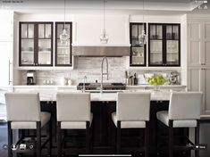 a kitchen with white chairs and marble counter tops in front of an island that has wine glasses on it