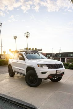 a white jeep parked on top of a parking lot next to palm trees and buildings