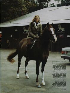 a woman riding on the back of a brown horse in front of a white building