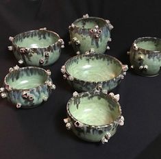 six green bowls with silver decorations on them sitting on a black tableclothed surface