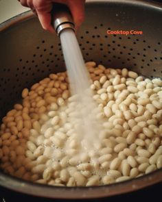 someone is sprinkling some white beans with a water faucet in a pot