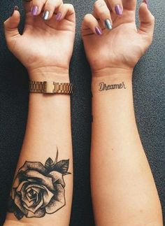 two women with matching tattoos on their arm and wrist, both holding hands up in the air