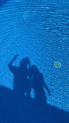 the shadow of two people standing in front of a swimming pool with blue tiles on it