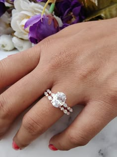 a woman's hand with a diamond ring on her left hand and flowers in the background