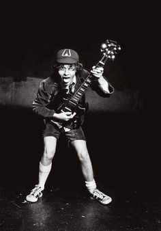 a man holding an electric guitar in his right hand and wearing a baseball cap on top of it