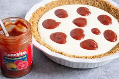 there is a pie with toppings next to a jar of jam