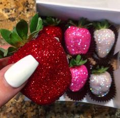 a hand is holding a strawberry with glitter on it and other strawberries in the background