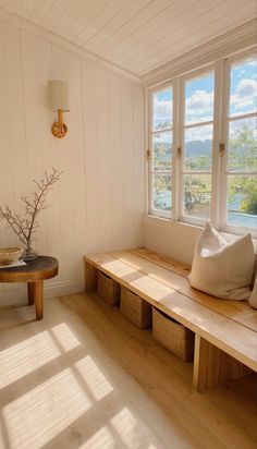 a wooden bench sitting next to a window in a room with white walls and wood flooring