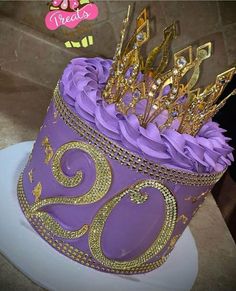 a purple and gold birthday cake with golden numbers on it's side, surrounded by other decorations