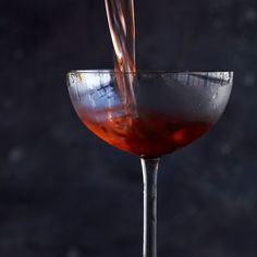 a glass filled with liquid being poured into the wine in front of a dark background