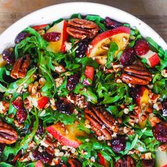 a salad with apples, cranberries and pecans in a white bowl on a wooden table