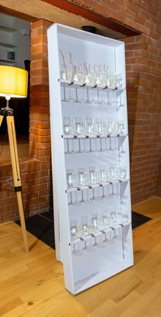 a display case filled with glasses on top of a hard wood floor next to a brick wall