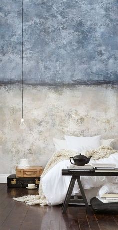 a bed with white sheets and pillows in front of a blue wall that has a painting on it