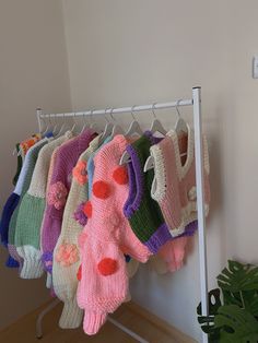 there are many knitted sweaters hanging on the rack next to a potted plant