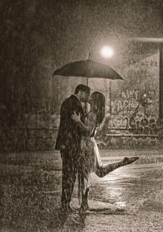 a man and woman kissing in the rain under an umbrella while holding each other's hands