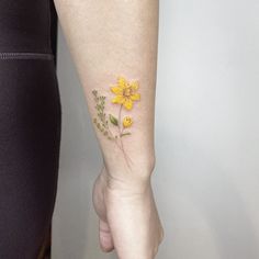 a woman's arm with a yellow flower tattoo on it