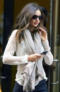 a woman wearing sunglasses and a scarf is looking at her cell phone while walking down the street