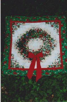 a quilted christmas wreath on the ground with red ribbon around it and green leaves