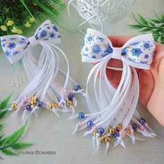 a hand is holding two small bows with beads on the ends and flowers in the background