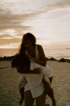 two people hug on the beach as the sun sets