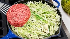 an iron skillet with shredded cabbage and a hamburger pattie being cooked in it