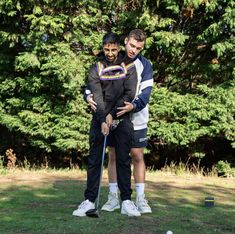 two young men standing next to each other on top of a lush green field with trees in the background