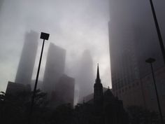 some tall buildings are in the fog on a cloudy day and there is no image here to provide a caption for