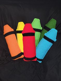 four crocheted fire extinguishers are lined up on a black background