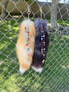 two furry key chains hanging on a chain link fence in the grass near a tree