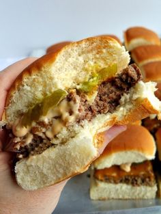 a hand holding a half eaten sandwich with meat, cheese and pickles on it