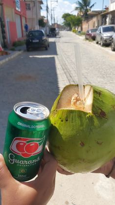 a person holding up a can of soda and a coconut