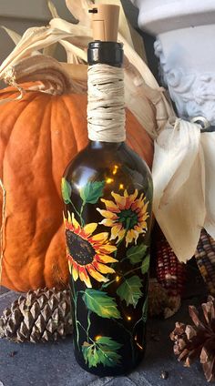 a bottle with sunflowers painted on it next to pumpkins and pine cones