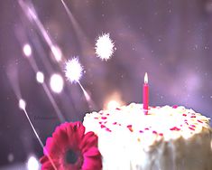 a birthday cake with white frosting and red flowers on the side, surrounded by sparklers