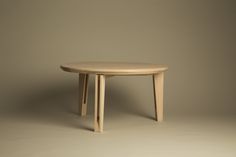 a round wooden table sitting on top of a white floor next to a gray wall