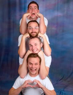 three men are sitting on top of each other making the shape of a heart with their hands